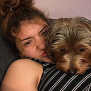 Loyalty is registered to the contest to win money with this photo: person, dog, face, pet, snuggling, close_up, indoor, quilted, comfort, sleepy, warmth, hair, striped_clothing, brown_hair, relaxed, cute, animal, friendship, expression, candid