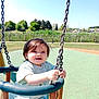 bench, blue_sky, casual_clothing, chain, child, daytime, fence, grass, greenery, happy, outdoor, park, person, playground, smiling, summer, sunny, swing, toddler, trees
