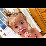 Paisley Mae is registered to the contest to win money with this photo: child, toddler, girl, portrait, face, smiling, eating, cake, frosting, dessert, messy_face, food, indoors, door, wooden_cabinet, bun_hair, hand, eyes, bare_shoulders, black_border