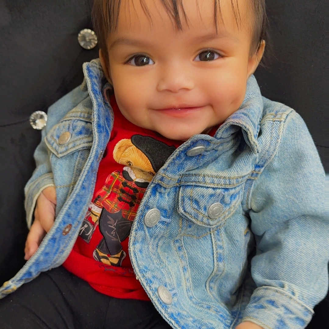 Zayanna joined the competition — help win amazing prizes! baby, black_pants, button, buttoned_jacket, child, clothing, cushioned_chair, cute, denim_jacket, face, hair, happy, indoor, person, pigtails, portrait, red_shirt, sitting, smile, young_child