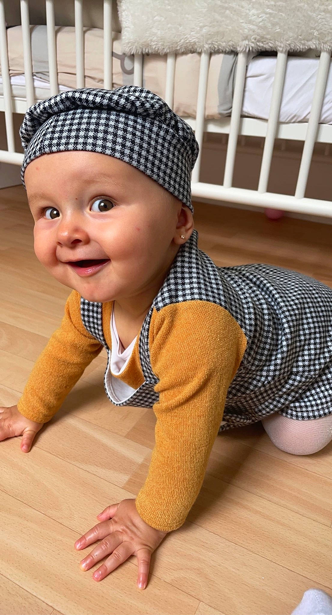 Tess a rejoint le concours — aidez-le/la à gagner de superbes lots ! baby, baby_toddler_clothing, cap, child, chin, face, facial_expression, flooring, happy, headgear, headwear, human_leg, joy, knee, leg, outerwear, person, skin, sleeve, smile