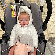 Romy participe au concours pour gagner de l'argent avec cette photo : baby, car_seat, stuffed_animal, toy, hoodie, white_clothing, pink, gray, floor_tiles, child, infant, blue_eyes, soft_toy, plush, seated, person, footwear, pants, indoor, cute