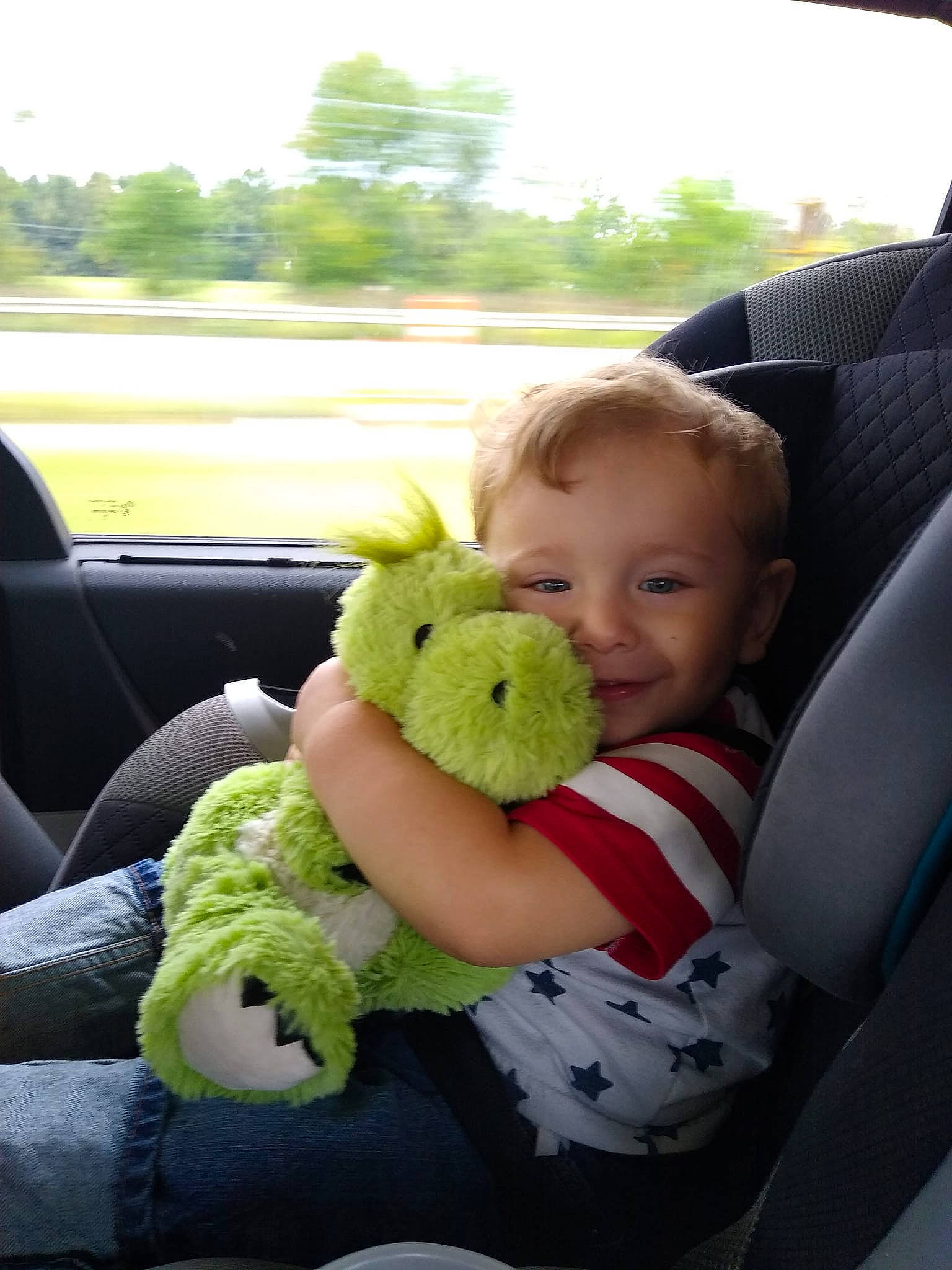 Brycen is registered to the contest to win money with this photo: baby_toddler_clothing, car, car_seat, chair, child, comfort, grass, happy, mammal, motor_vehicle, person, skin, sky, smile, stuffed_toy, thumb, toddler, toy, tree, vehicle_door