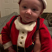 Theodore joined the competition — help win amazing prizes! baby, child, santa_claus_costume, red_clothing, hat, indoor, person, hand, cat, furniture, couch, door, sleeping_cat, cute, holiday, festive, portrait, infant, smile, holding