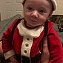 baby, child, santa_claus_costume, red_clothing, hat, indoor, person, hand, cat, furniture, couch, door, sleeping_cat, cute, holiday, festive, portrait, infant, smile, holding