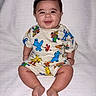 baby, smiling, sitting, child, infant, clothing, sesame_street, colorful, cute, happy, portrait, indoors, blanket, footwearless, shorts, tshirt, person, young_child, skin, face