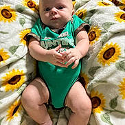 Richard Jr is registered to the contest to win money with this photo: baby, infant, child, blanket, sunflower_pattern, green_onesie, cute, hands, legs, skin, face, expression, lying_down, indoors, soft_texture, comfort, adorable, portrait, newborn, curious