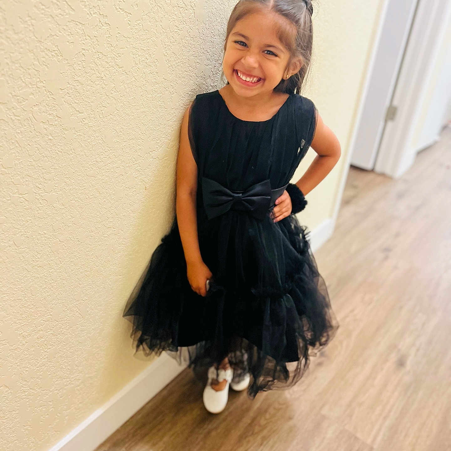 Vaani Kaur is registered to the contest to win money with this photo: child, girl, smile, dress, black_dress, bow, hair_bow, indoor, hallway, floor, wood_floor, wall, textured_wall, white_shoes, happy, posing, fashion, person, cute, portrait