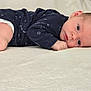 baby, newborn, infant, lying_down, blanket, onesie, navy_blue, stars, face, hand, curious, soft_texture, closeup, portrait, child, young, sleepwear, resting, indoors, cute