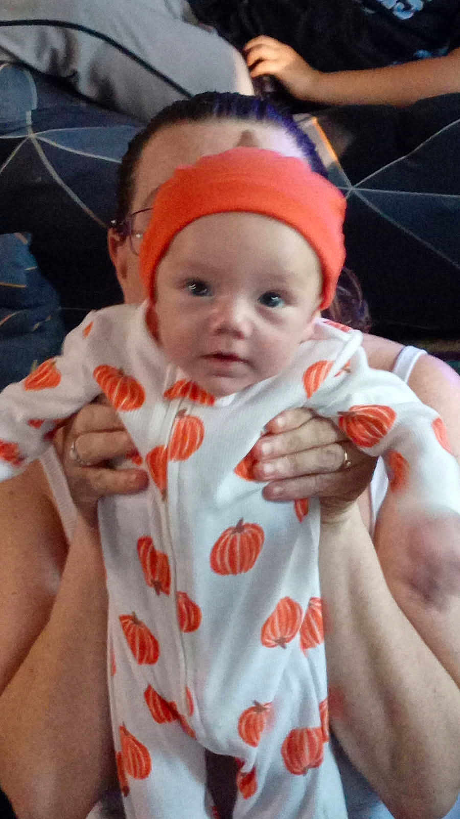 Taylon is registered to the contest to win money with this photo: baby, infant, pumpkin, onesie, hat, orange, white, person, hands, holding, indoor, couch, blurred_background, clothing, face, headwear, child, cute, portrait, toddler