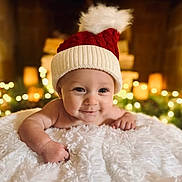 Lincoln joined the competition — help win amazing prizes! baby, infant, smiling, face, hat, knit_hat, pom_pom, blanket, soft_texture, holiday_lights, bokeh, warm_lighting, cozy, cute, portrait, indoors, child, happy, festive, christmas