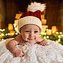 baby, infant, smiling, face, hat, knit_hat, pom_pom, blanket, soft_texture, holiday_lights, bokeh, warm_lighting, cozy, cute, portrait, indoors, child, happy, festive, christmas