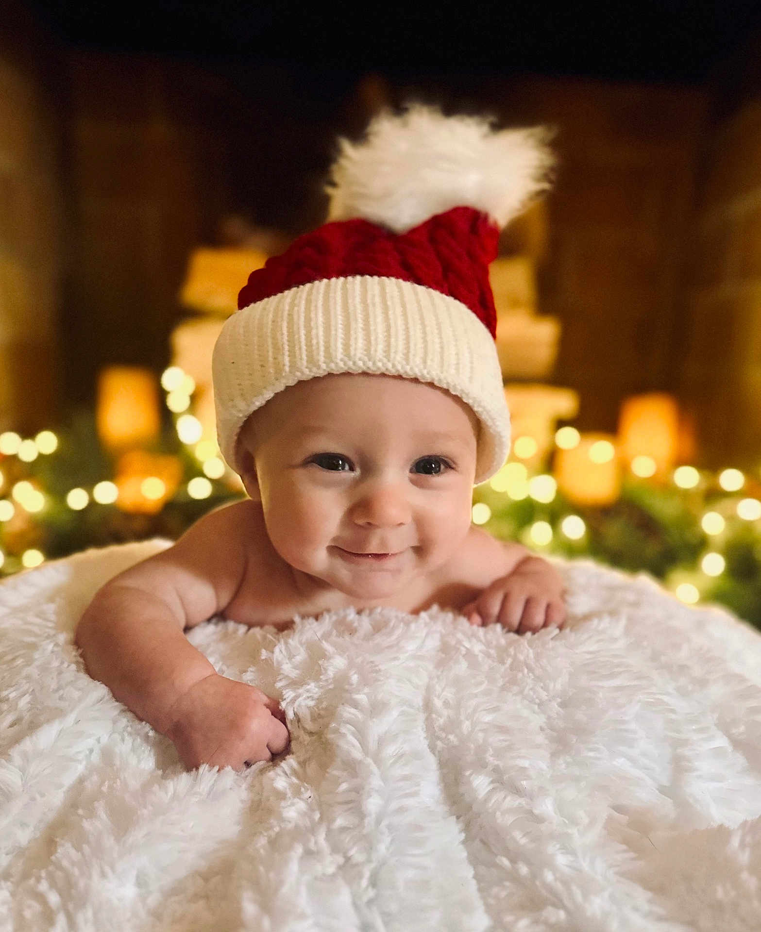 Lincoln joined the competition — help win amazing prizes! baby, infant, smiling, face, hat, knit_hat, pom_pom, blanket, soft_texture, holiday_lights, bokeh, warm_lighting, cozy, cute, portrait, indoors, child, happy, festive, christmas