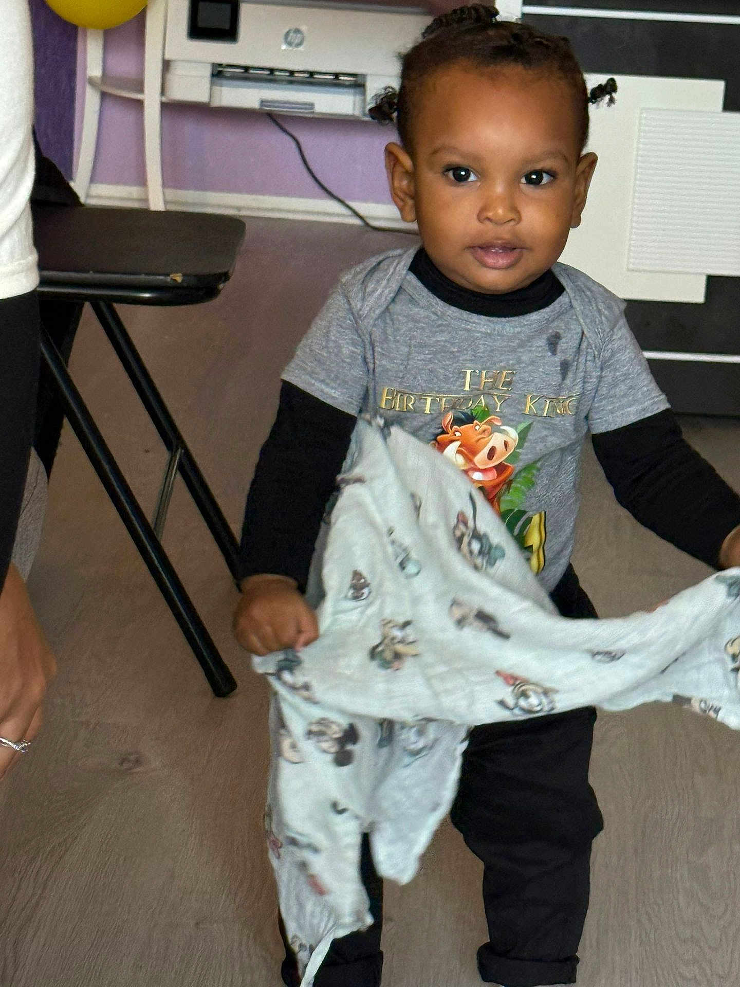 Djahnaël a rejoint le concours — aidez-le/la à gagner de superbes lots ! toddler, child, indoor, blanket, braided_hair, shirt, black_pants, floor, curious, standing, person, home, furniture, table, wall, cable, expression, young_child, clothing, portrait