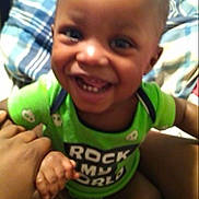 Rayjarious joined the competition — help win amazing prizes! bed, blanket, child, clothing, comfort, cute, face, green_shirt, hand, happy, indoor, infant, joyful, person, plaid, room, sitting, smiling, toddler, young_child