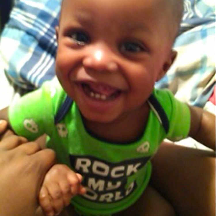 Rayjarious joined the competition — help win amazing prizes! bed, blanket, child, clothing, comfort, cute, face, green_shirt, hand, happy, indoor, infant, joyful, person, plaid, room, sitting, smiling, toddler, young_child