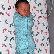 William is registered to the contest to win money with this photo: baby, newborn, infant, swaddle, sleeping, crib, mattress, footprint_pattern, bedding, mesh_side, zipper, blue_clothing, nursery, indoors, portrait, peaceful, top_view, blanket, cot, small_person