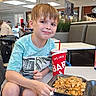 child, boy, food_court, fried_rice, shrimp, drink, table, bench, smile, casual_clothing, shorts, sneakers, indoor, restaurant, people, shopping_mall, light_brown_hair, happy, meal, plastic_container