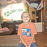 child, boy, smile, orange_shirt, jeans, indoor, seated, casual, furniture, television, blurred_background, wood_floor, home, happy, portrait, person, young, short_hair, under_armour, confident