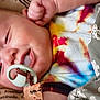 baby, pacifier, tie_dye, colorful, blanket, cactus_pattern, close_up, infant, face, smile, child, sleepy, cozy, fabric, soft_focus, person, newborn, cute, resting, comfort