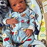 baby, infant, blanket, onesie, blue_clothing, baby_seat, patterned_clothing, food_characters, cute, young_child, indoors, colorful, comfort, face, hand, footed_pajamas, soft_texture, portrait, child, newborn