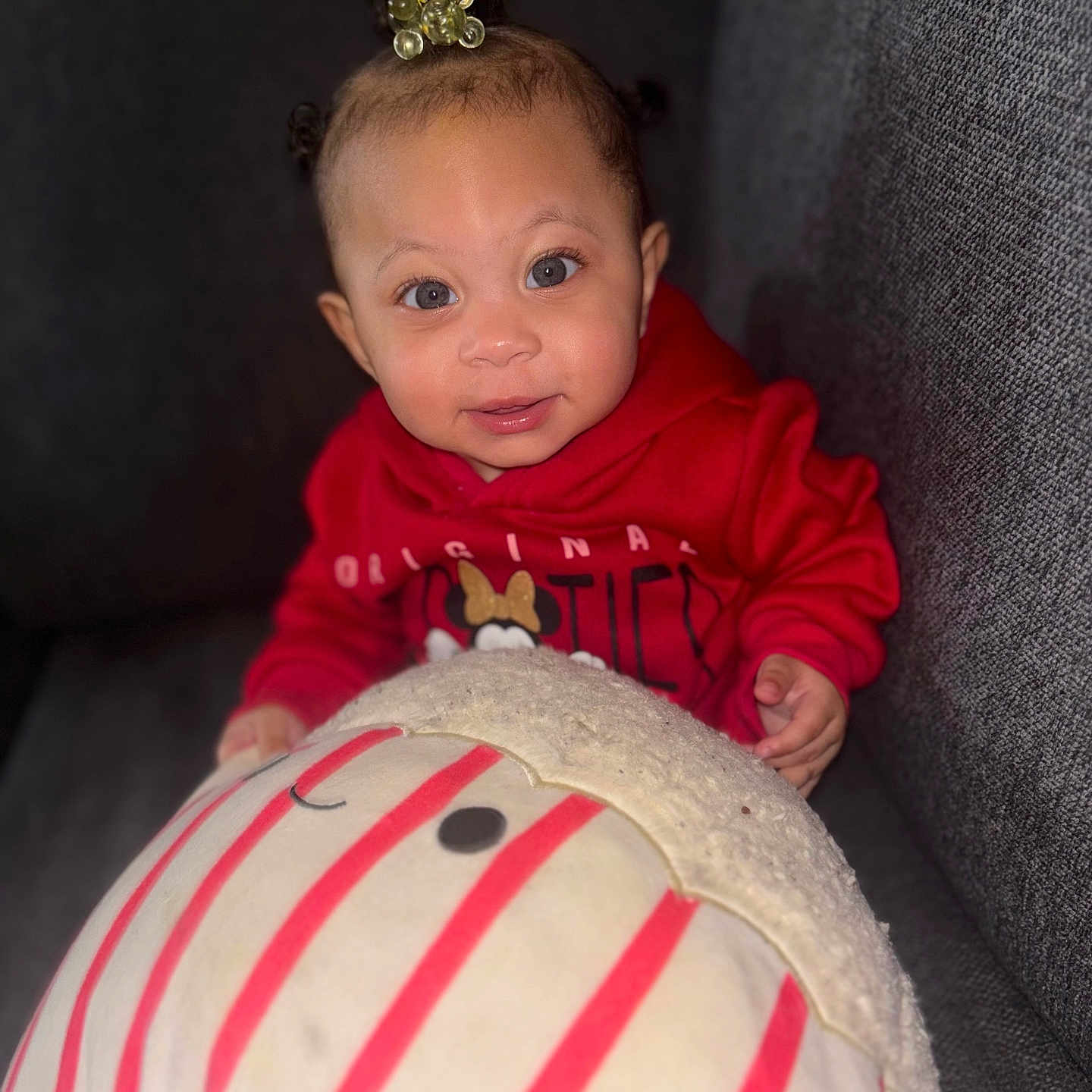 Laniyah joined the competition — help win amazing prizes! baby, casual, child, couch, cozy, cute, face, happy, hoodie, indoor, infant, person, plush_toy, portrait, red_clothing, seated, smile, soft_toy, striped, young_child