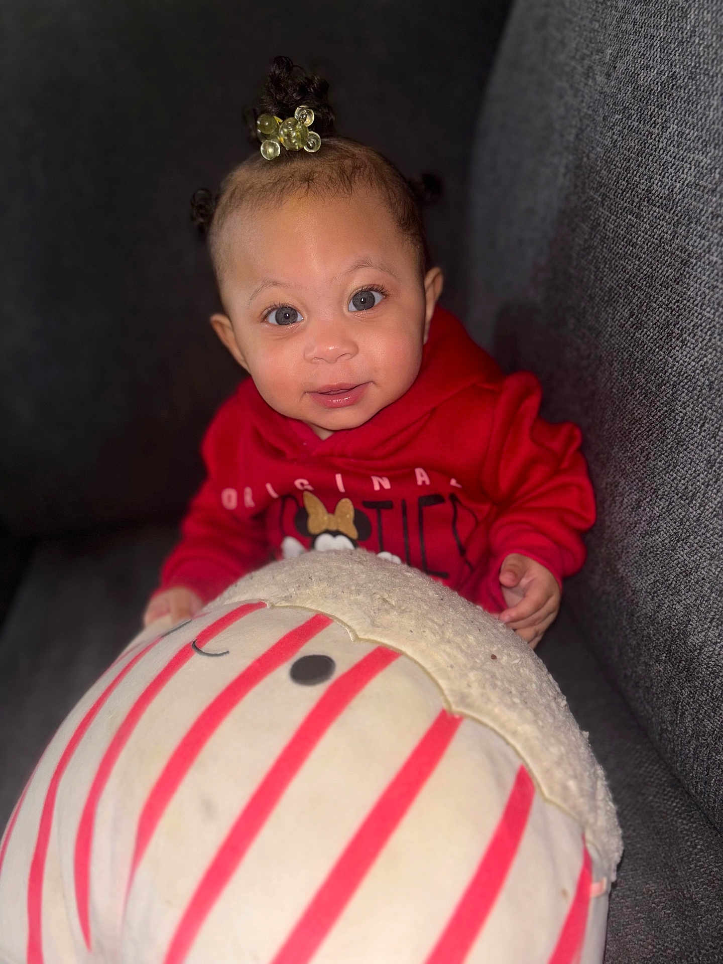 Laniyah joined the competition — help win amazing prizes! baby, child, hoodie, red_clothing, plush_toy, smile, face, couch, indoor, cute, young_child, person, soft_toy, striped, seated, happy, cozy, casual, portrait, infant