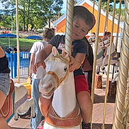 Théo a rejoint le concours — aidez-le/la à gagner de superbes lots ! child, boy, carousel, carousel_horse, amusement_park, outdoor, daylight, clothing, red_shorts, marvel_tshirt, hat, pole, people, trees, building, smile, fun, ride, toy, play
