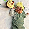baby, infant, cupcake, birthday_candle, headband, flower, green_outfit, blanket, smile, celebration, first_birthday, sweet, cute, lying_down, small_hands, soft_texture, food, dessert, cream, happy