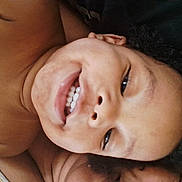 Nylah is registered to the contest to win money with this photo: child, smile, face, teeth, curly_hair, close_up, portrait, happy, skin, lying_down, bare_shoulders, expression, person, young, cute, joy, natural_light, casual, relaxed, indoors