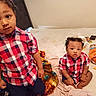 child, toddler, baby, plaid_shirt, matching_outfits, bed, blanket, snack, cheese_puffs, messy_room, indoor, curious, sitting, standing, person, hair, face, clothing, expression, casual