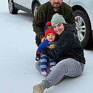 Xander joined the competition — help win amazing prizes! family, baby, child, adult_male, adult_female, snow, winter, beanie_hat, striped_outfit, mittens, smile, cuddle, parked_car, wheel, sitting, portrait, outdoors, cold_weather, casual_clothes, cozy