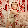 baby, infant, smiling, standing, onesie, heart, valentine_text, ribbon_bows, pink_background, furry_stool, stool, fur_rug, studio_shot, decorations, cute, chubby_legs, rosy_cheeks, portrait, happy, baby_face