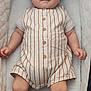 baby, infant, child, romper, striped_clothing, padded_bassinet, white_bassinet, lying_down, barefoot, cute, young_child, comfort, sleeping_area, indoor, portrait, small_hands, small_feet, neutral_expression, light_skin_tone, clothing