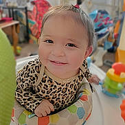 Aurora is registered to the contest to win money with this photo: baby, child, infant, smiling, portrait, face, indoors, playroom, activity_seat, toy, colorful, leopard_print, clothing, sitting, happy, playful, home, furniture, close_up, photography