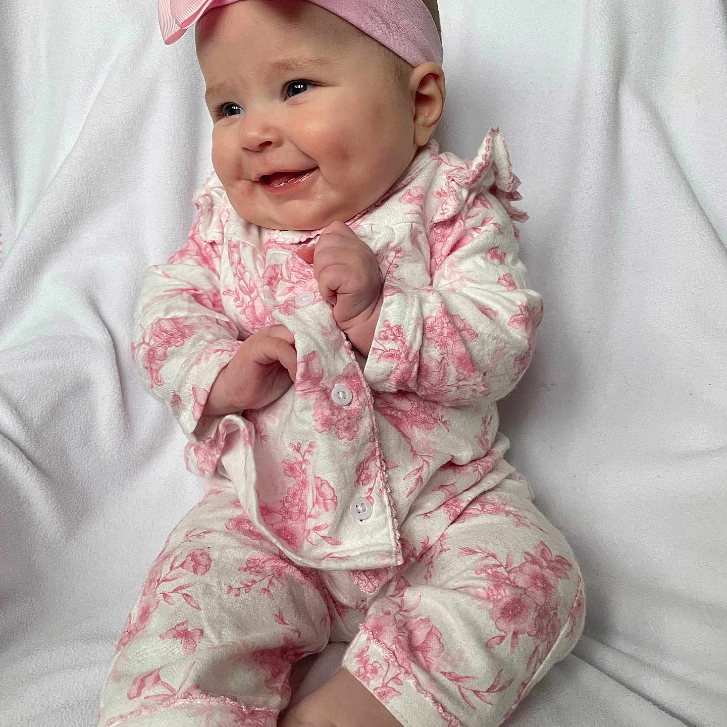 Delcie joined the competition — help win amazing prizes! baby, child, clothing, cute, dimples, face, floral_outfit, hands, happy, headband, indoors, infant, pink_bow, portrait, sitting, skin, smiling, soft_texture, white_blanket, young