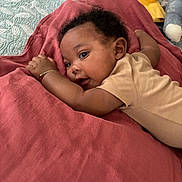Tafari joined the competition — help win amazing prizes! baby, infant, child, blanket, quilt, plush_toy, bracelet, lying_down, indoors, curly_hair, person, cute, soft_lighting, cozy, bedroom, clothing, resting, face, skin, smiling