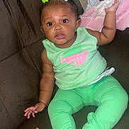 Dior is registered to the contest to win money with this photo: baby, child, infant, green_clothing, bows, couch, brown_couch, tattooed_hand, hand, reflection, mirror, blanket, pink_blanket, indoor, person, cute, sitting, curious, family, home