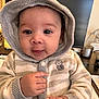 baby, hoodie, child, face, hands, indoor, computer_monitor, desk, candle, paper, clothing, curious, cute, portrait, sitting, striped, knitwear, owl_emblem, tongue, young_child