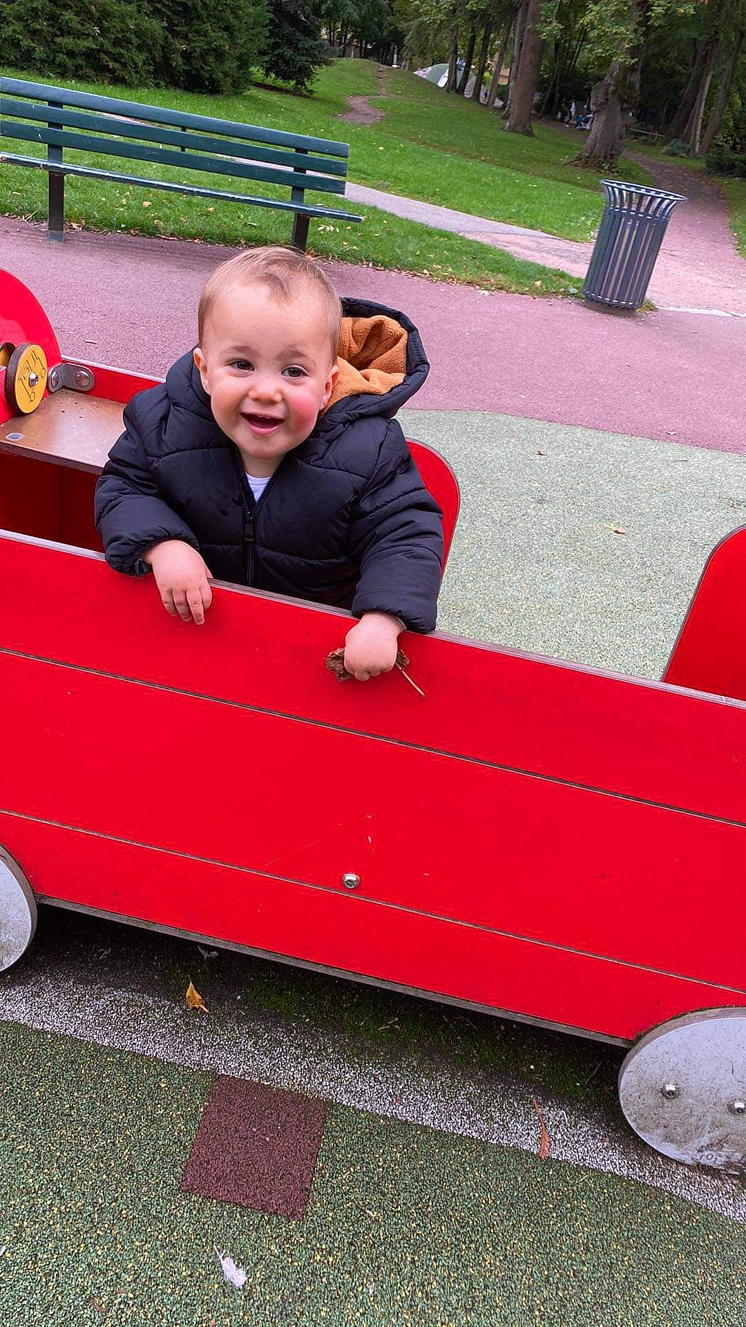 Lenny a rejoint le concours — aidez-le/la à gagner de superbes lots ! automotive_exterior, baby, baby_toddler_clothing, bench, child, city, fun, grass, leisure, motor_vehicle, person, plant, public_space, rolling, sitting, sleeve, smile, tire, toddler, vehicle