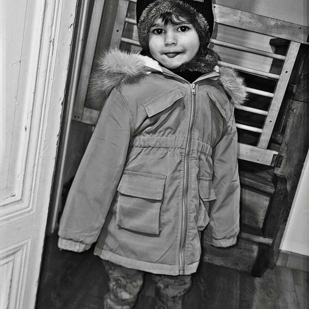 Juliann participe au concours pour gagner de l'argent avec cette photo : child, kid, winter_coat, hat, indoor, doorway, smile, standing, floor, wooden_floor, jacket, fur_hood, shoes, pants, portrait, person, young, cute, warm_clothing, black_and_white