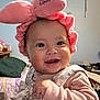 Luz is registered to the contest to win money with this photo: baby, infant, smiling, pink_headband, bunny_ears, bow, floral, clothing, hand, face, indoors, bedroom, blanket, pillow, furniture, cute, happy, person, child, portrait