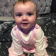 Elena is registered to the contest to win money with this photo: baby, infant, pink_clothing, cute, face, eyes, hands, sitting, bed, blanket, pattern, star_pattern, headboard, tuft_of_hair, indoors, portrait, child, soft_lighting, curious, chubby