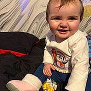 Elena is registered to the contest to win money with this photo: baby, child, smiling, face, clothing, boots, hair_bow, sitting, bed, blanket, toy, hand, wall, pattern, indoors, cute, festive, penguin, colorful, happy