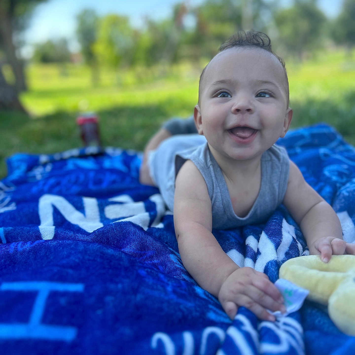 Azariah joined the competition — help win amazing prizes! baby, blanket, blue_sky, child, clothing, cute, daytime, face, grass, happy, infant, nature, outdoor, playful, portrait, relaxing, smiling, sunlight, toy, young_child