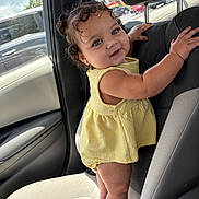 Maisie joined the competition — help win amazing prizes! toddler, child, car_interior, car_seat, yellow_dress, curly_hair, standing, holding, window, daylight, happy, cute, person, portrait, automobile, seat, interior, skin, smile, baby