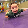 baby, casual_clothing, child, curly_hair, cute, expression, face, floor, happy, head, hoodie, indoor, infant, person, playroom, portrait, purple_mat, skin, smiling, young_child