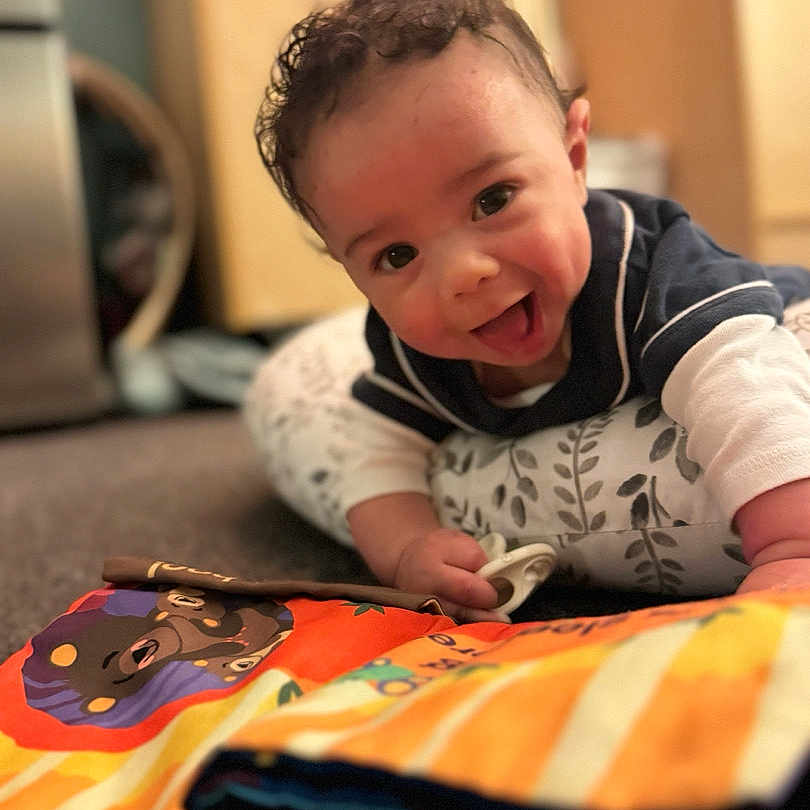 Wayland is registered to the contest to win money with this photo: applique, baby, babylaughing, blanket, bodypart, clothing, face, finger, hand, happy, head, laughing, pants, person, photography, portrait, quilt, sitting, smile, t_shirt