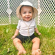 Wayland is registered to the contest to win money with this photo: baby, baby_clothes, barefoot, bucket_hat, child, cute, fence, grass, greenery, happy, hat, nature, outdoor, playful, portrait, sitting, smiling, summer, sunlight, young_child