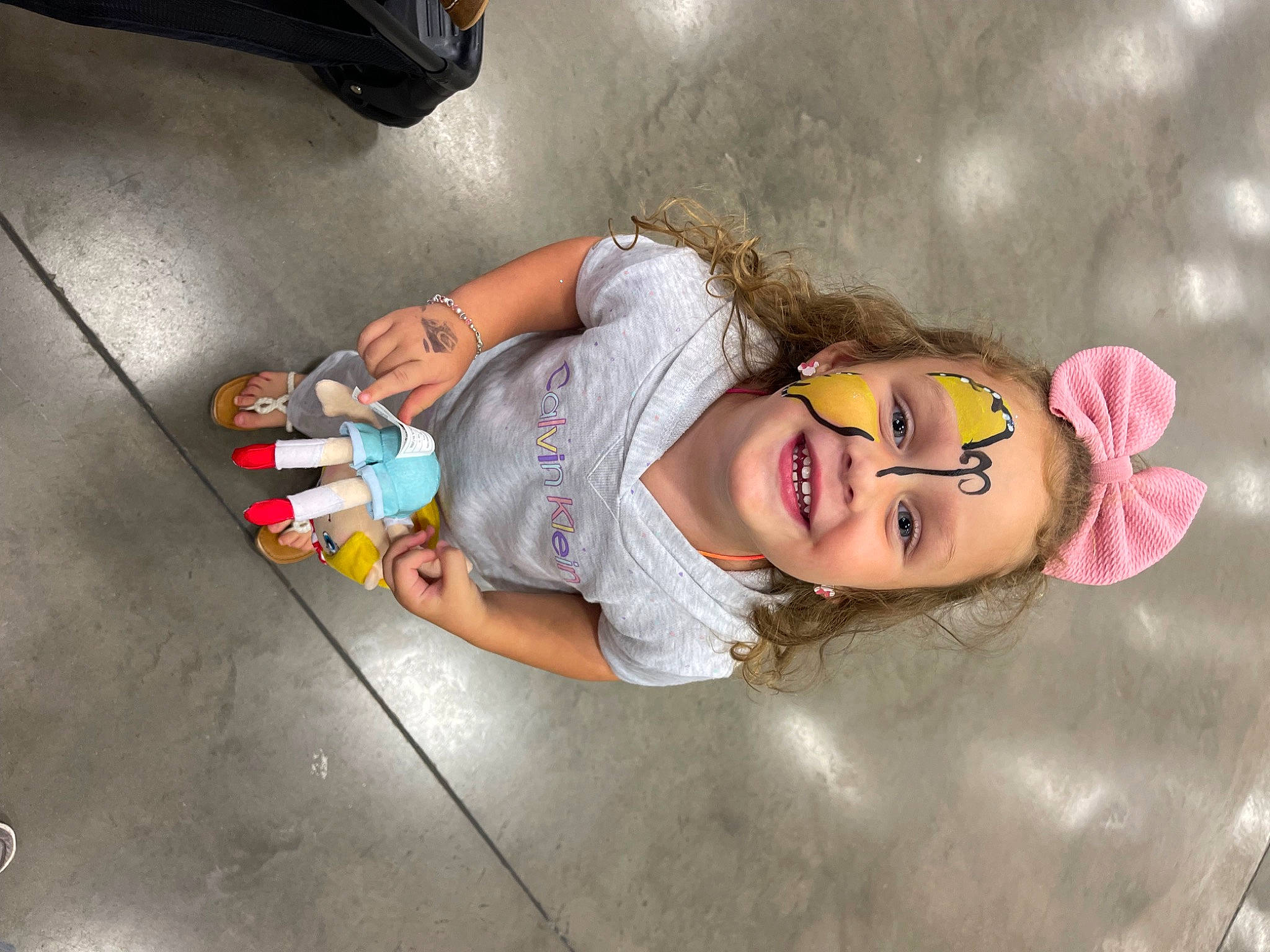 Willow is registered to the contest to win money with this photo: automotive_exterior, bumper, child, eyewear, flooring, fun, happy, human_leg, joy, leg, leisure, person, room, sandal, shoe, sitting, sneakers, t_shirt, thigh, toddler